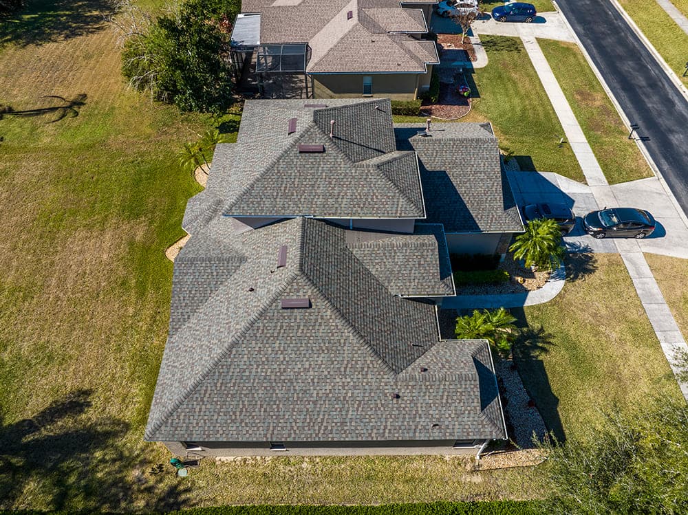 Aerial view of a gray shingle roof with multiple gables and a screened pool enclosure